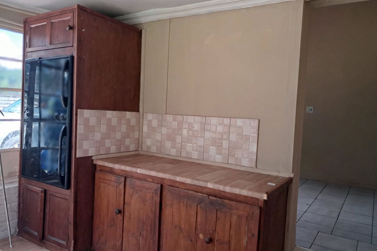 A dated kitchen area featuring built-in wooden cabinetry, a laminate countertop, and a tiled backsplash, offering potential for a modern renovation.