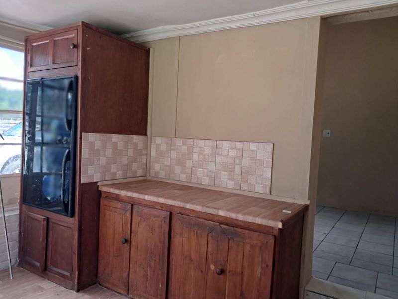 A dated kitchen area featuring built-in wooden cabinetry, a laminate countertop, and a tiled backsplash, offering potential for a modern renovation.
