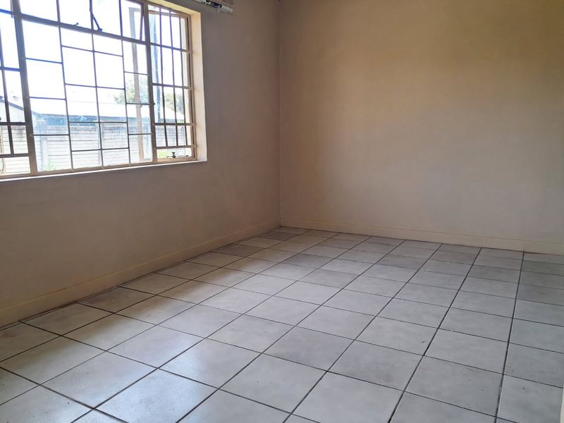 An empty bedroom featuring tiled flooring and metal security bars on the window, providing a blank canvas for potential interior design updates.
