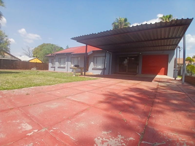 Front exterior view of a single-story house featuring a large paved driveway, attached carport, and a single garage.