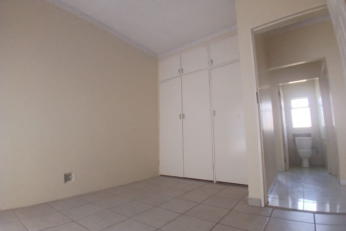 An empty bedroom featuring built-in cupboards, tiled flooring, and a ceiling fan, with an adjacent view into a bathroom.