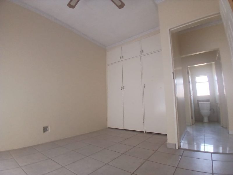 An empty bedroom featuring built-in cupboards, tiled flooring, and a ceiling fan, with an adjacent view into a bathroom.
