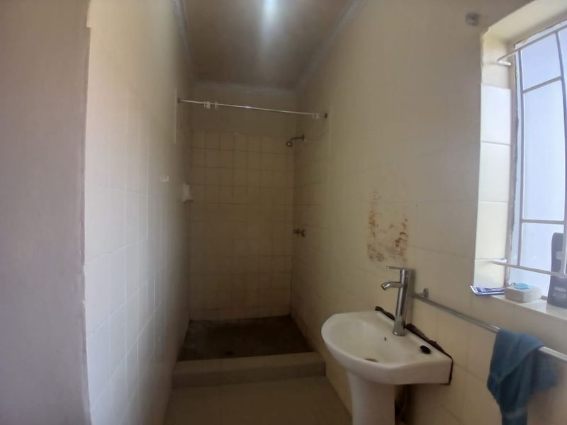 A dated bathroom featuring a pedestal basin and a shower cubicle, requiring cosmetic updates and repairs to wall finishes.