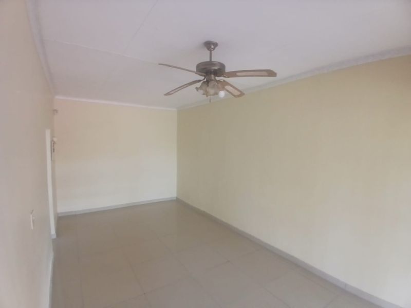 An empty living room featuring tiled flooring, a ceiling fan, and neutral wall finishes, offering a blank canvas for personalization.