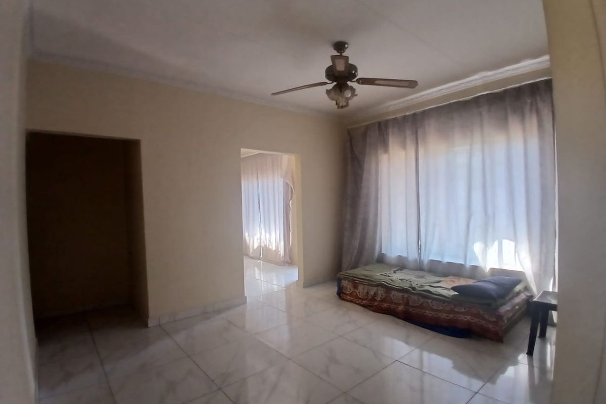 A spacious living area featuring tiled flooring, a ceiling fan, and coved ceiling details, offering a neutral canvas for interior design.