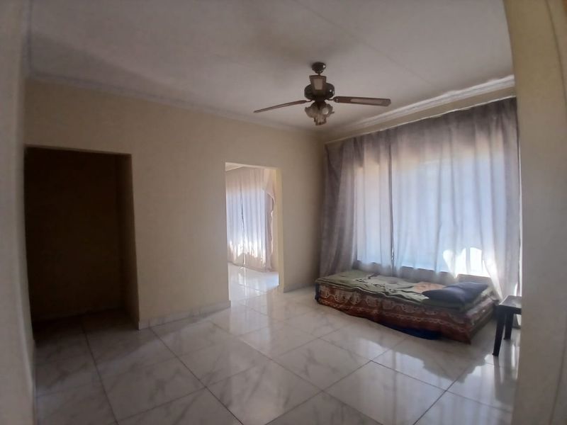 A spacious living area featuring tiled flooring, a ceiling fan, and coved ceiling details, offering a neutral canvas for interior design.