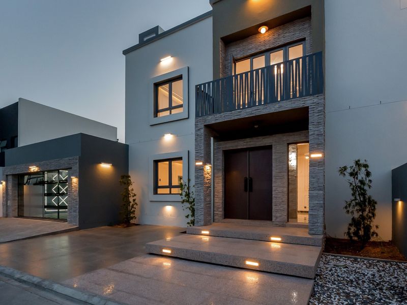 Modern double-story residence featuring stone cladding, a private balcony, integrated exterior lighting, and a paved driveway with a secure garage.