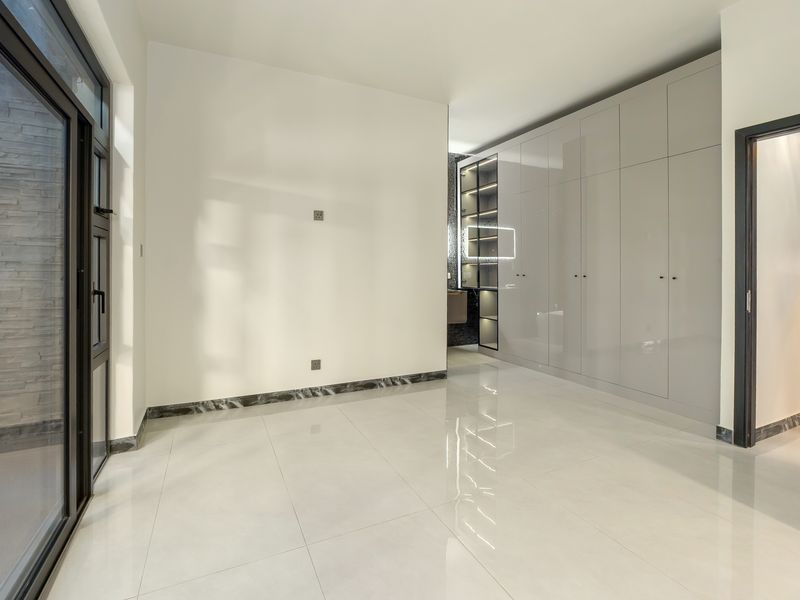 A modern, empty bedroom featuring high-gloss built-in cupboards, polished tiled flooring, marble skirting, and a large sliding glass door providing natural light.