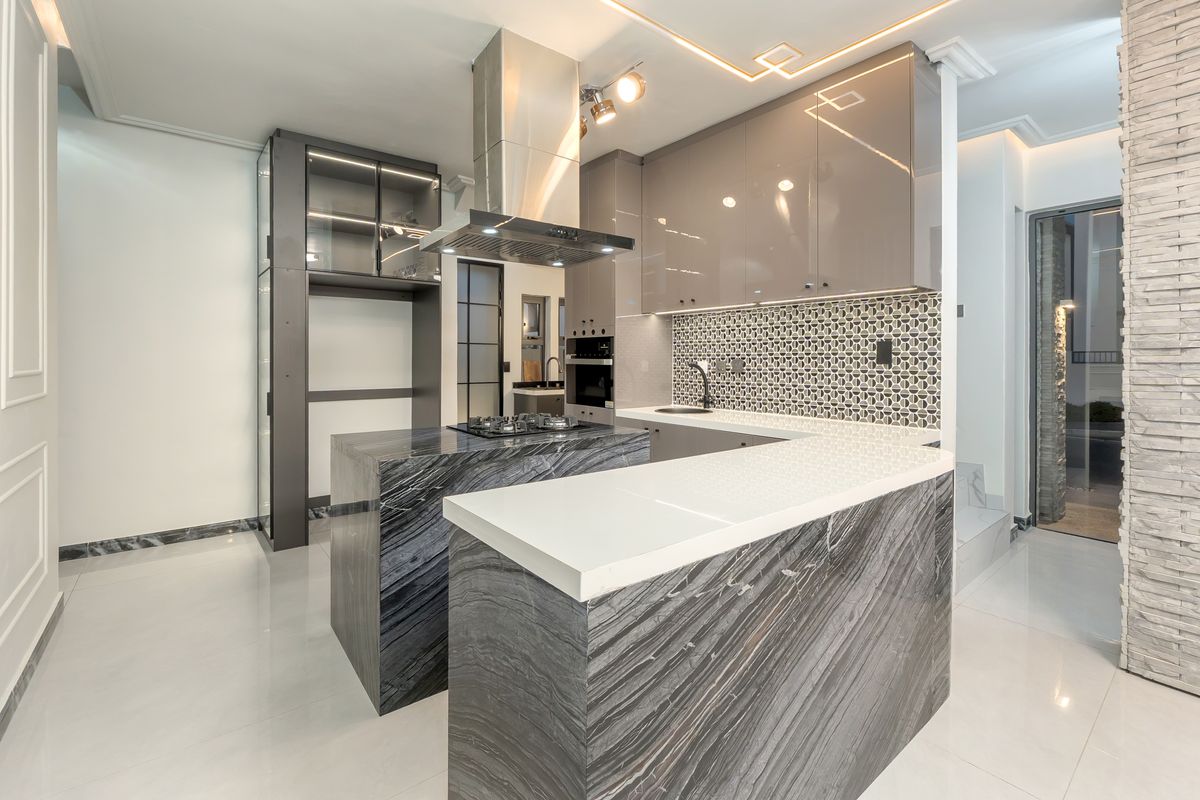 Modern kitchen featuring high-end marble island, sleek glossy cabinetry, integrated appliances, and a stylish mosaic tile backsplash with contemporary recessed lighting.