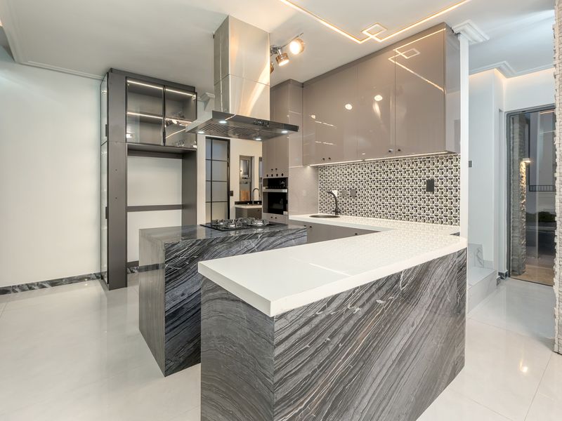 Modern kitchen featuring high-end marble island, sleek glossy cabinetry, integrated appliances, and a stylish mosaic tile backsplash with contemporary recessed lighting.