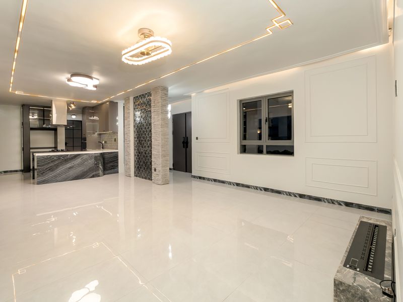 Spacious open-plan living and kitchen area featuring high-end marble finishes, modern recessed lighting, decorative wall molding, and a sleek built-in fireplace.