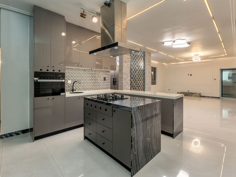 Modern open-plan kitchen featuring high-gloss grey cabinetry, a stone-topped island with integrated gas hob, and premium marble-look flooring throughout the living space.