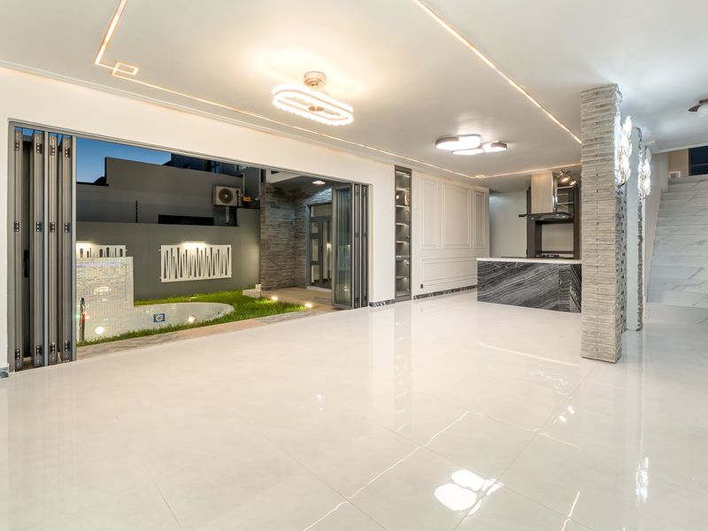 Spacious open-plan living area featuring high-end marble-look flooring, modern recessed lighting, a stone-clad pillar, and seamless indoor-outdoor flow through large bi-fold doors.
