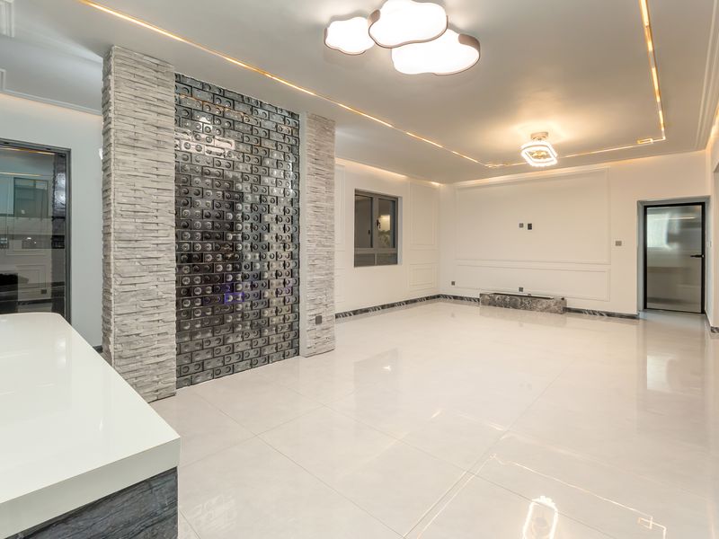 Spacious living area featuring elegant porcelain flooring, decorative stone and glass block feature walls, recessed ceiling lighting, and sophisticated wainscoting details.