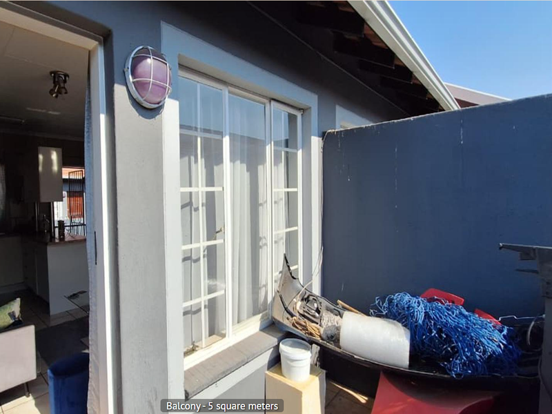 A compact balcony area featuring tiled flooring, an exterior wall light, and access to the interior living space through a sliding glass door.