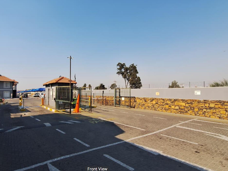 Front view of the apartment complex entrance featuring a paved driveway, security guard house, and stone-clad perimeter wall.