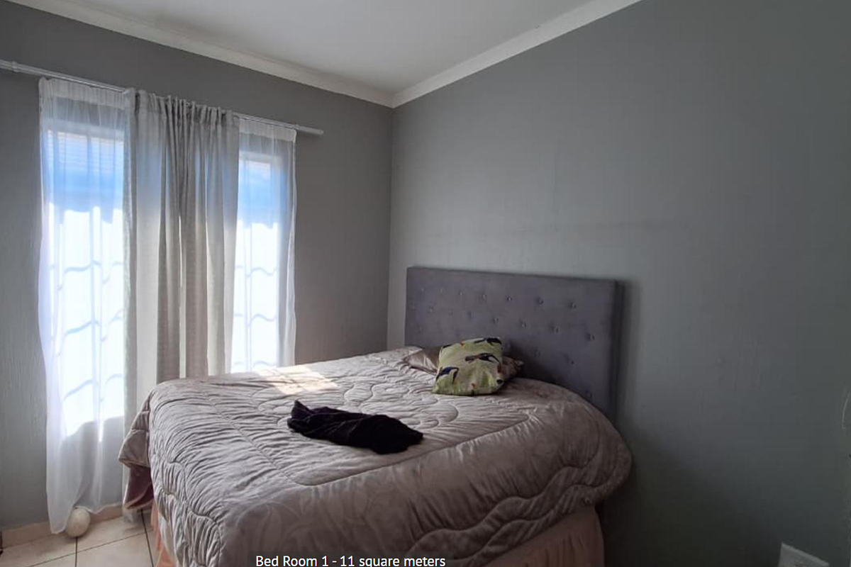 A bedroom featuring tiled flooring and neutral grey walls, providing a functional space with natural light from the window.