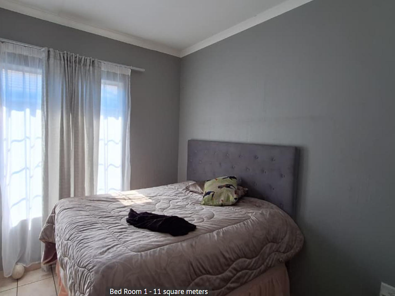 A bedroom featuring tiled flooring and neutral grey walls, providing a functional space with natural light from the window.