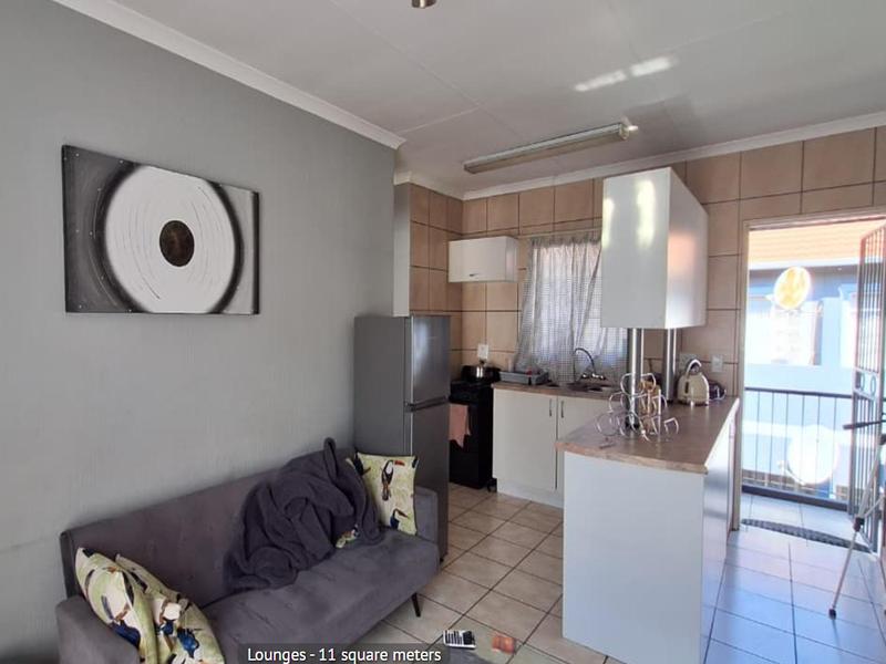 Open plan living and kitchen area featuring tiled flooring, functional cabinetry, and direct access to a balcony through a security gate.