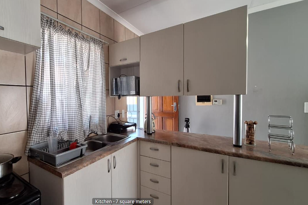 A functional kitchen featuring light-toned cabinetry, laminate countertops, a double basin sink, and a breakfast bar with a tiled backsplash.