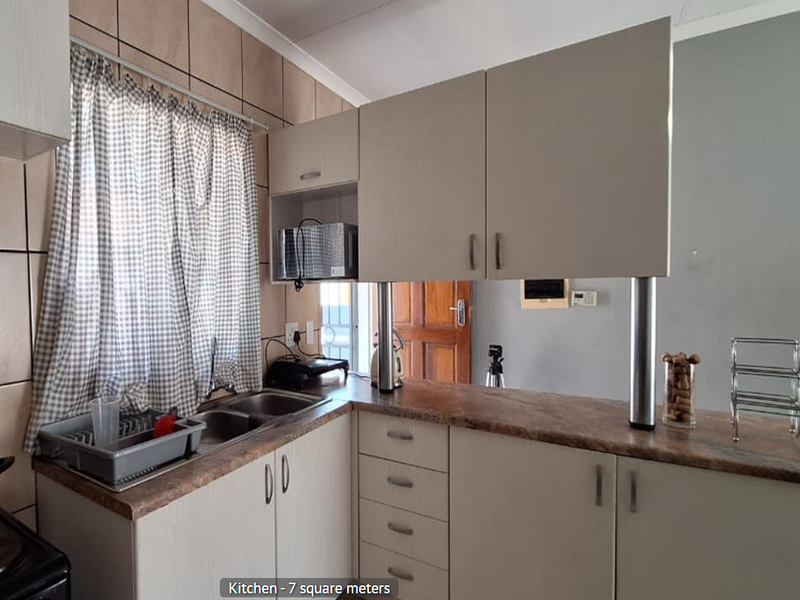 A functional kitchen featuring light-toned cabinetry, laminate countertops, a double basin sink, and a breakfast bar with a tiled backsplash.