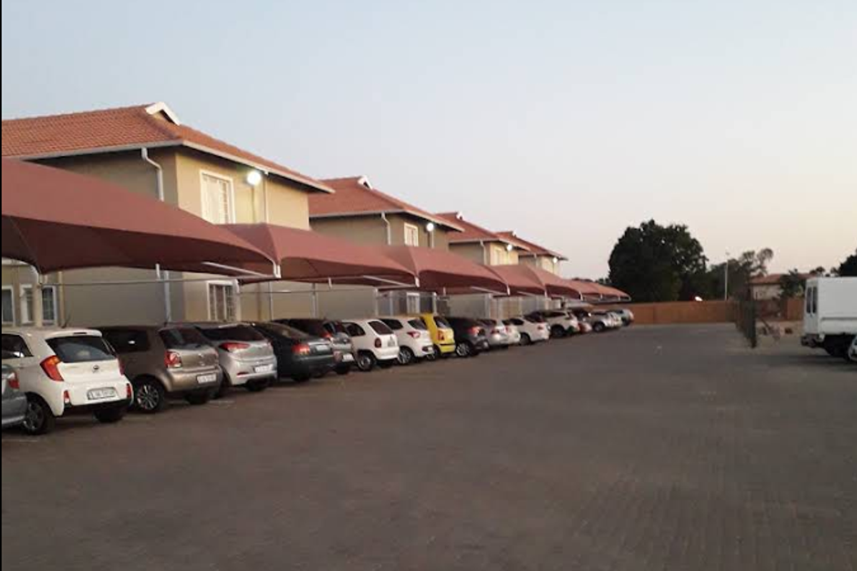 Exterior view of the apartment complex featuring a paved parking area with covered shade cloth carports for residents.
