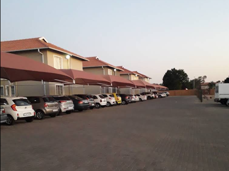 Exterior view of the apartment complex featuring a paved parking area with covered shade cloth carports for residents.