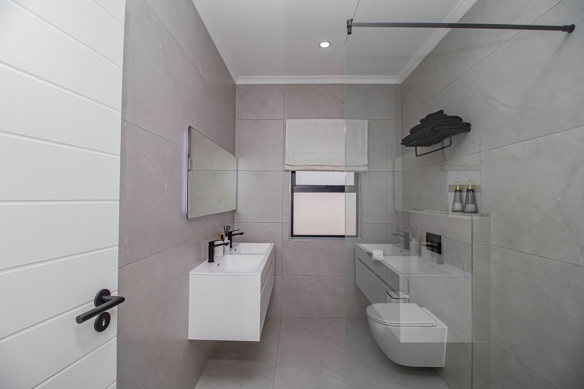 Modern bathroom featuring a wall-mounted double vanity, wall-hung toilet, glass shower screen, and contemporary grey large-format tiling with black fixtures.
