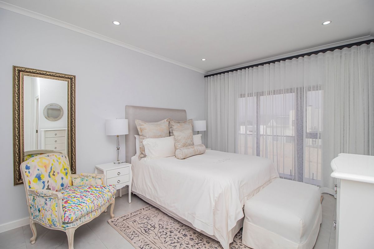 A well-maintained bedroom featuring neutral tones, tiled flooring, recessed downlighting, and a large sliding glass door with floor-to-ceiling curtains.