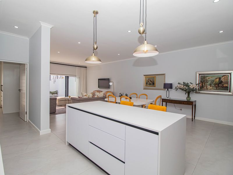 Spacious open-plan living and dining area featuring a modern kitchen island, neutral tiled flooring, and contemporary pendant lighting.