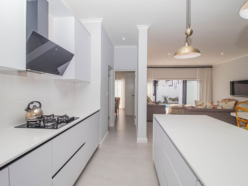 Modern open-plan kitchen featuring sleek white cabinetry, a gas hob with extractor, and a central island, flowing seamlessly into the living area.