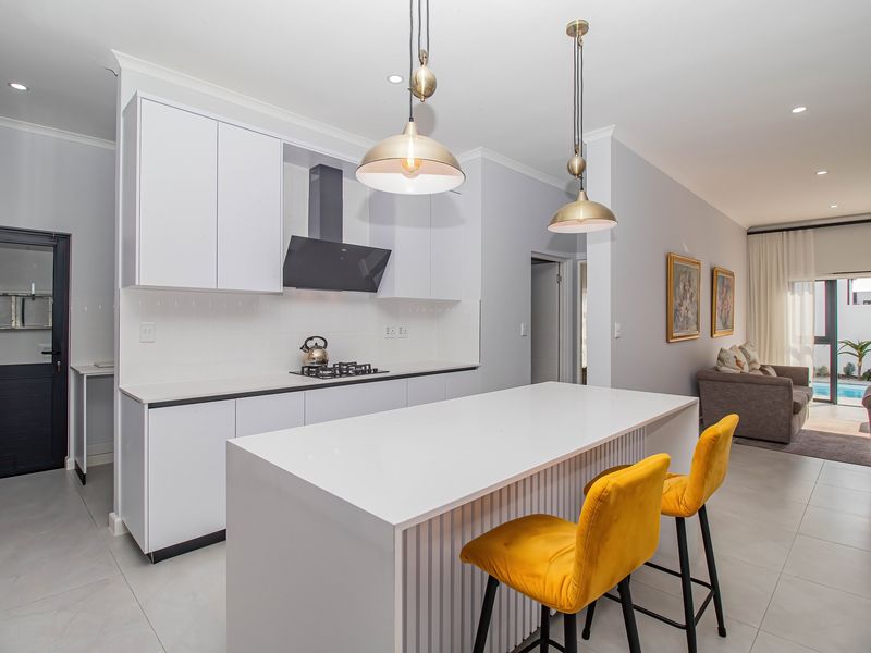 Modern open-plan kitchen featuring a central island, sleek white cabinetry, gas hob, and integrated extractor, flowing seamlessly into the adjacent living area.