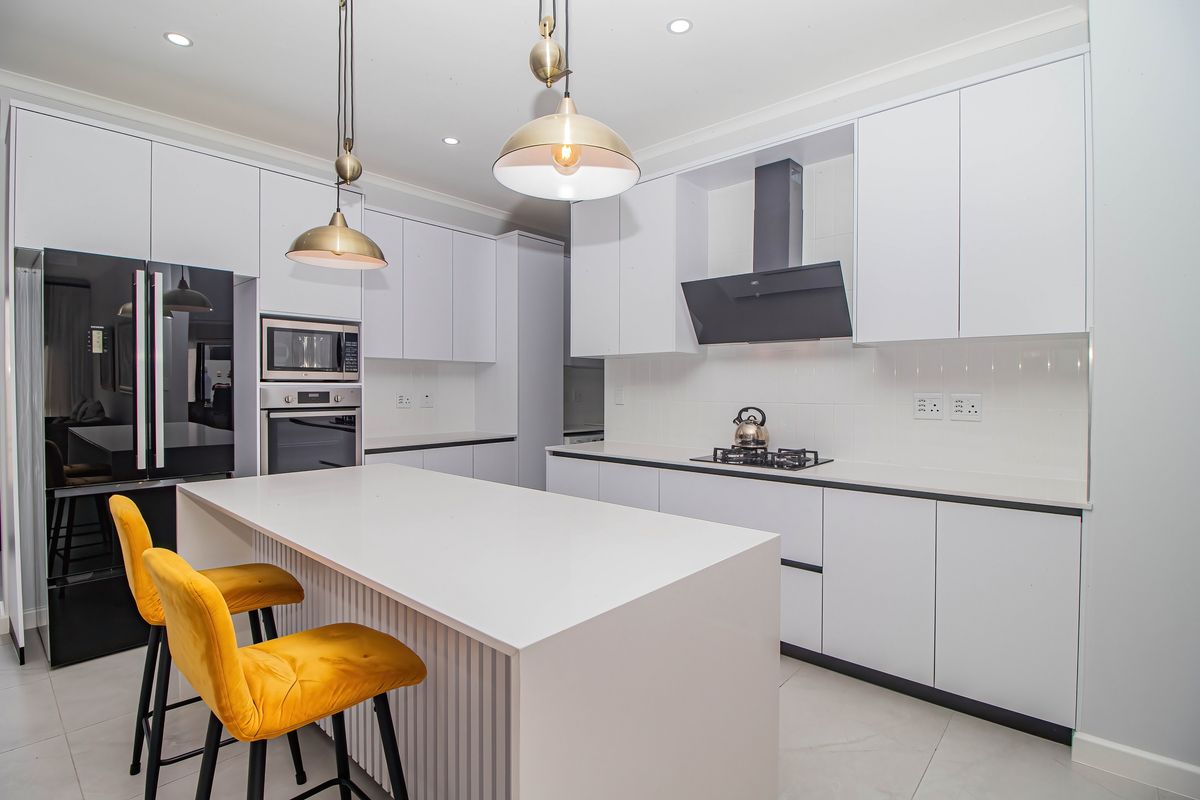 Modern kitchen featuring white cabinetry, a central island, built-in oven and microwave, gas hob with extractor fan, and sleek tiled flooring.