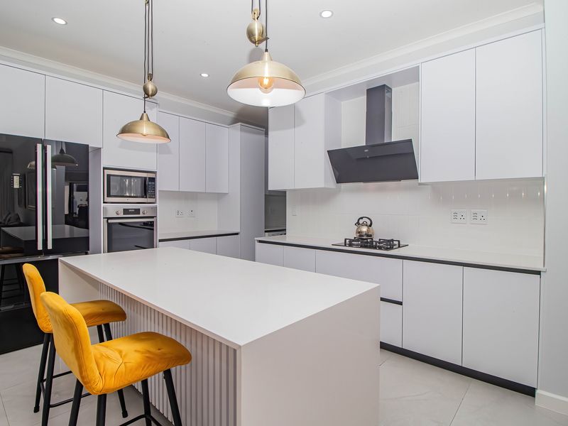Modern kitchen featuring white cabinetry, a central island, built-in oven and microwave, gas hob with extractor fan, and sleek tiled flooring.