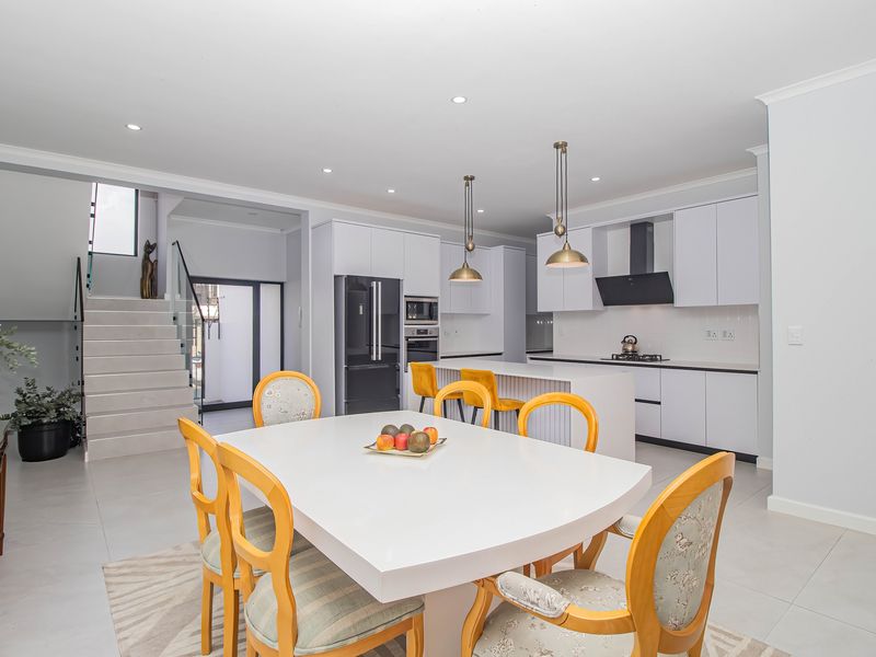 Modern open-plan kitchen and dining area featuring a central island, sleek cabinetry, integrated appliances, and a contemporary staircase with glass balustrade.