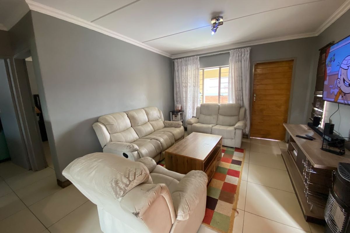 A comfortable living room featuring tiled flooring, neutral wall tones, and classic cornicing, providing a functional and well-lit space for relaxation.