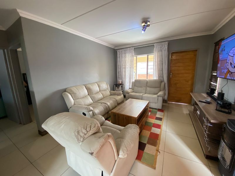 A comfortable living room featuring tiled flooring, neutral wall tones, and classic cornicing, providing a functional and well-lit space for relaxation.