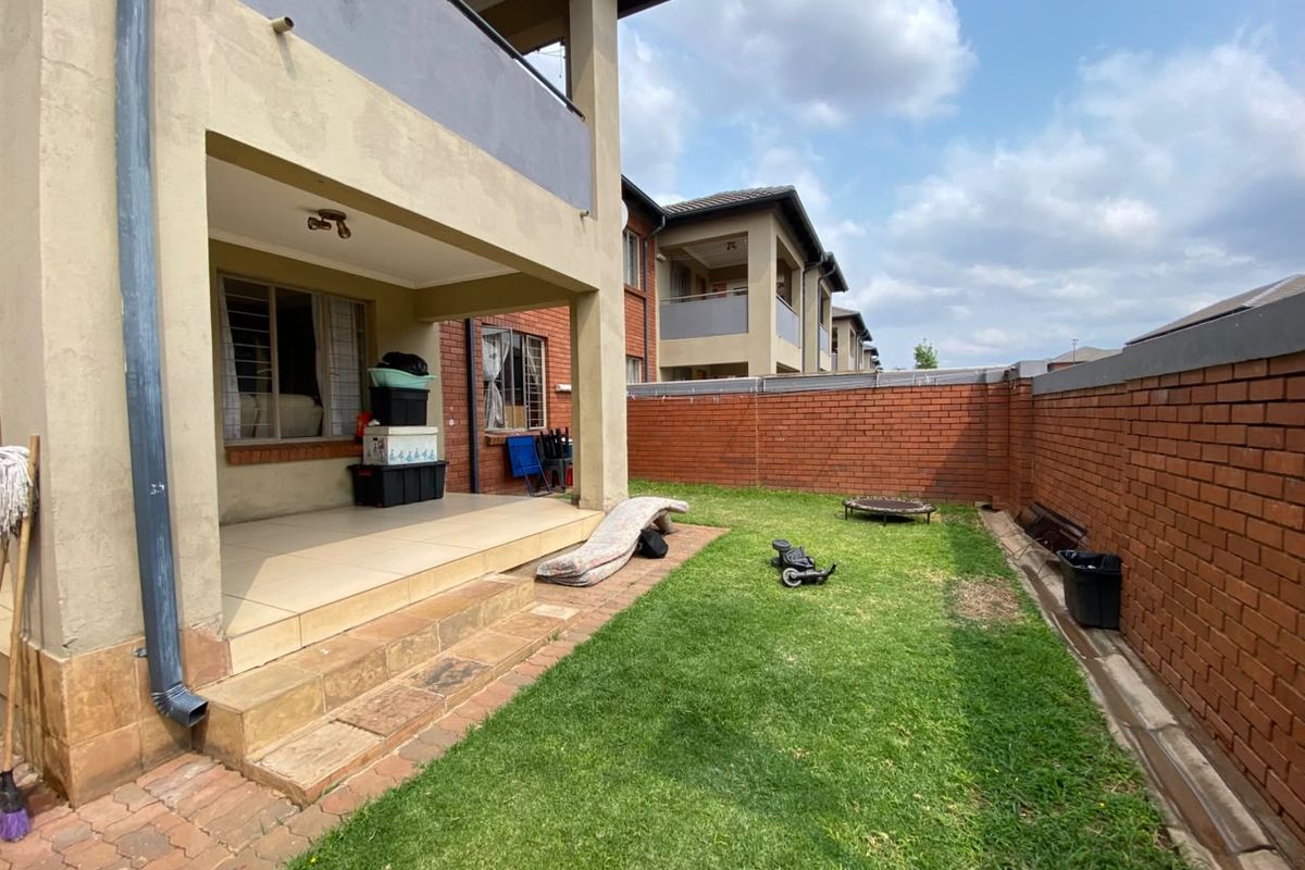 Rear view of the apartment featuring a covered patio with tiled flooring, stone steps, and a private garden enclosed by a brick boundary wall.