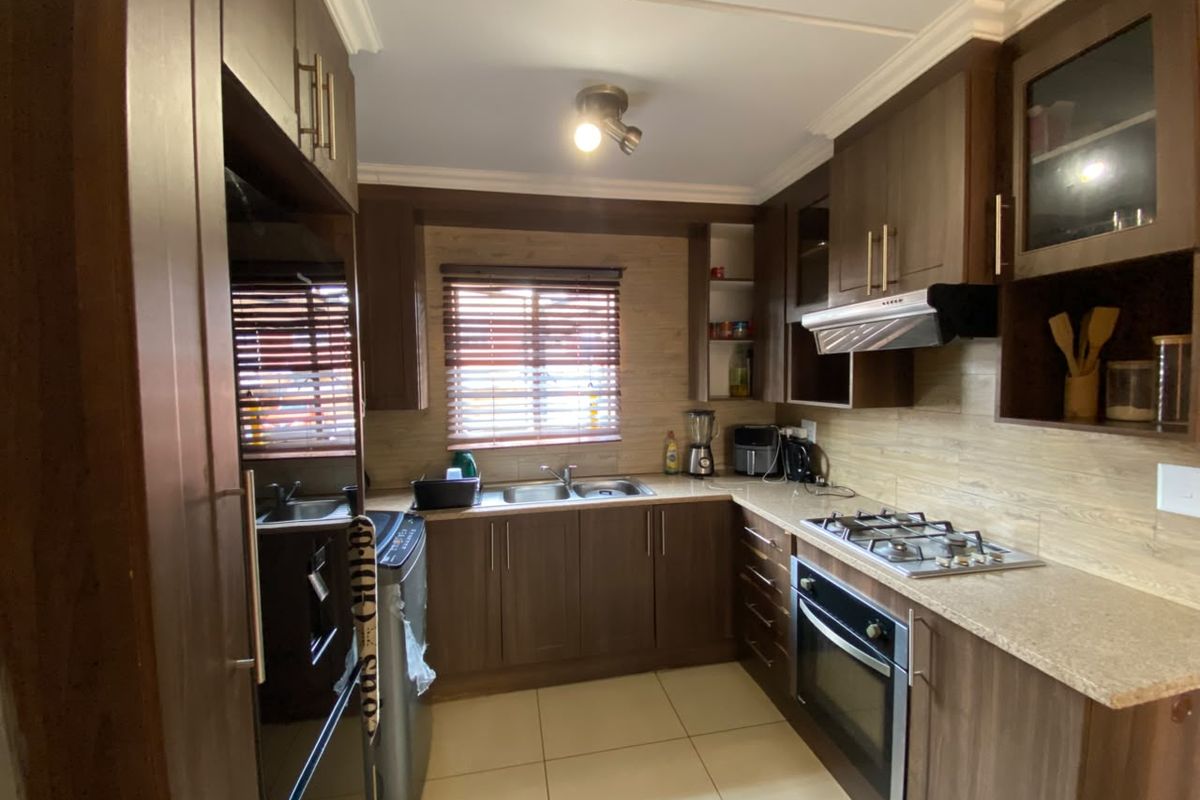 A functional kitchen featuring dark wood cabinetry, stone-look laminate countertops, a gas hob, built-in oven, and tiled flooring with neutral wall finishes.