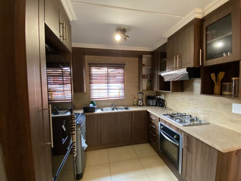 A functional kitchen featuring dark wood cabinetry, stone-look laminate countertops, a gas hob, built-in oven, and tiled flooring with neutral wall finishes.