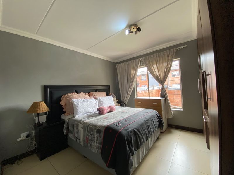 A bedroom featuring tiled flooring, built-in cupboards, and a ceiling-mounted spotlight, offering a functional and well-maintained living space.