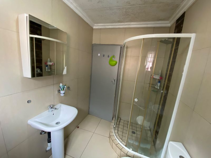 A compact bathroom featuring a pedestal basin, a corner shower enclosure with a glass door, and a mirrored medicine cabinet with tiled finishes.