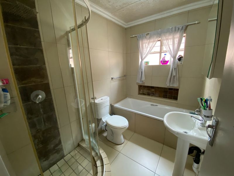 A functional bathroom featuring a shower enclosure, bathtub, pedestal basin, and toilet with neutral wall and floor tiling.