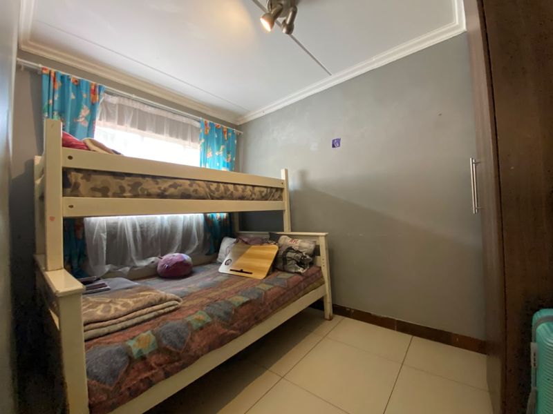 A compact bedroom featuring tiled flooring, a built-in cupboard, and a window with natural light.