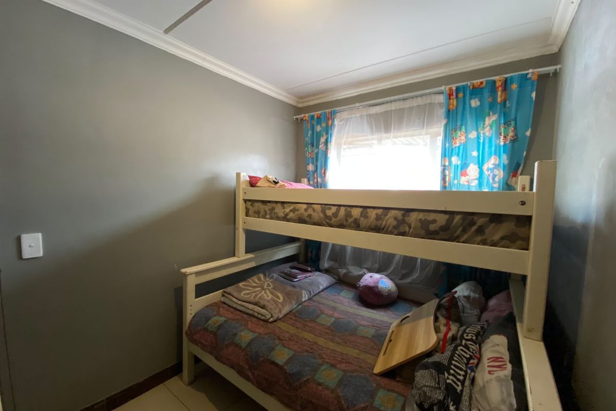 A compact bedroom featuring tiled flooring and crown molding, providing a functional space for a child or guest room.