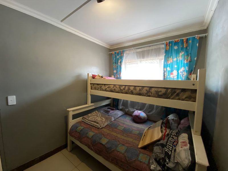 A compact bedroom featuring tiled flooring and crown molding, providing a functional space for a child or guest room.