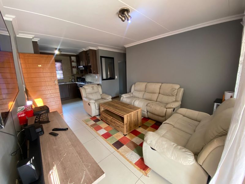 Open plan living area featuring tiled flooring and a connected kitchen with built-in cabinetry and an extractor fan.