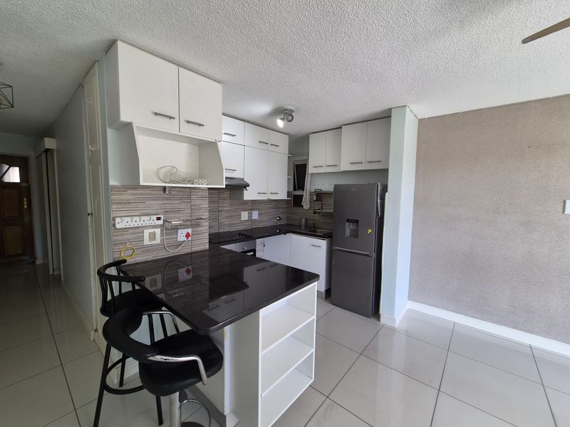 Compact kitchen featuring granite countertops, white cabinetry, a breakfast nook, and tiled flooring, offering a functional layout for apartment living.