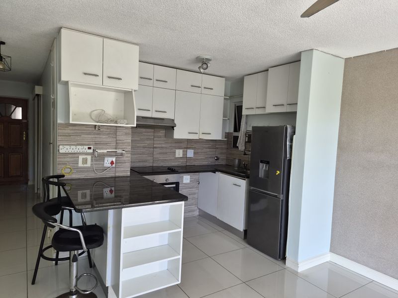 Compact kitchen featuring white built-in cabinetry, granite countertops, an electric hob, and an integrated breakfast nook with tiled flooring.