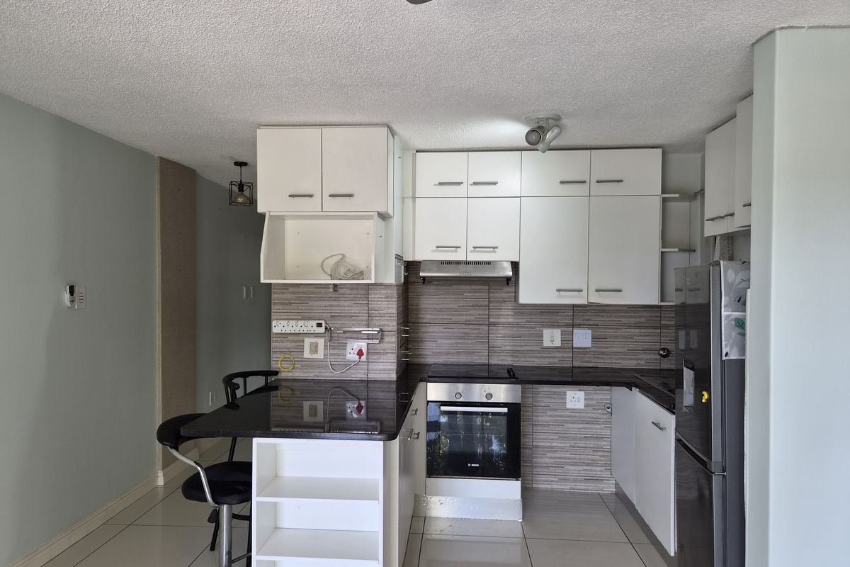 Compact kitchen featuring white cabinetry, dark laminate countertops, built-in oven and hob, tiled backsplash, and a functional breakfast bar area.